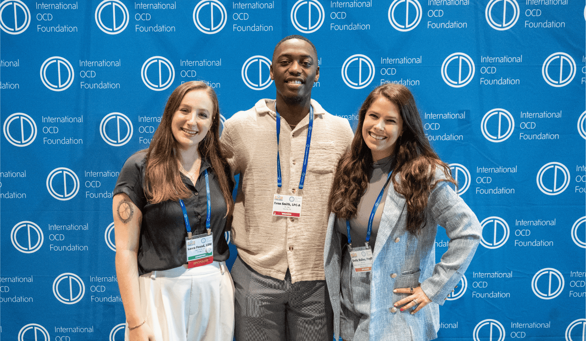 3 people two woman and a man posing in front of a backdrop with the IOCDF Logo repeating over